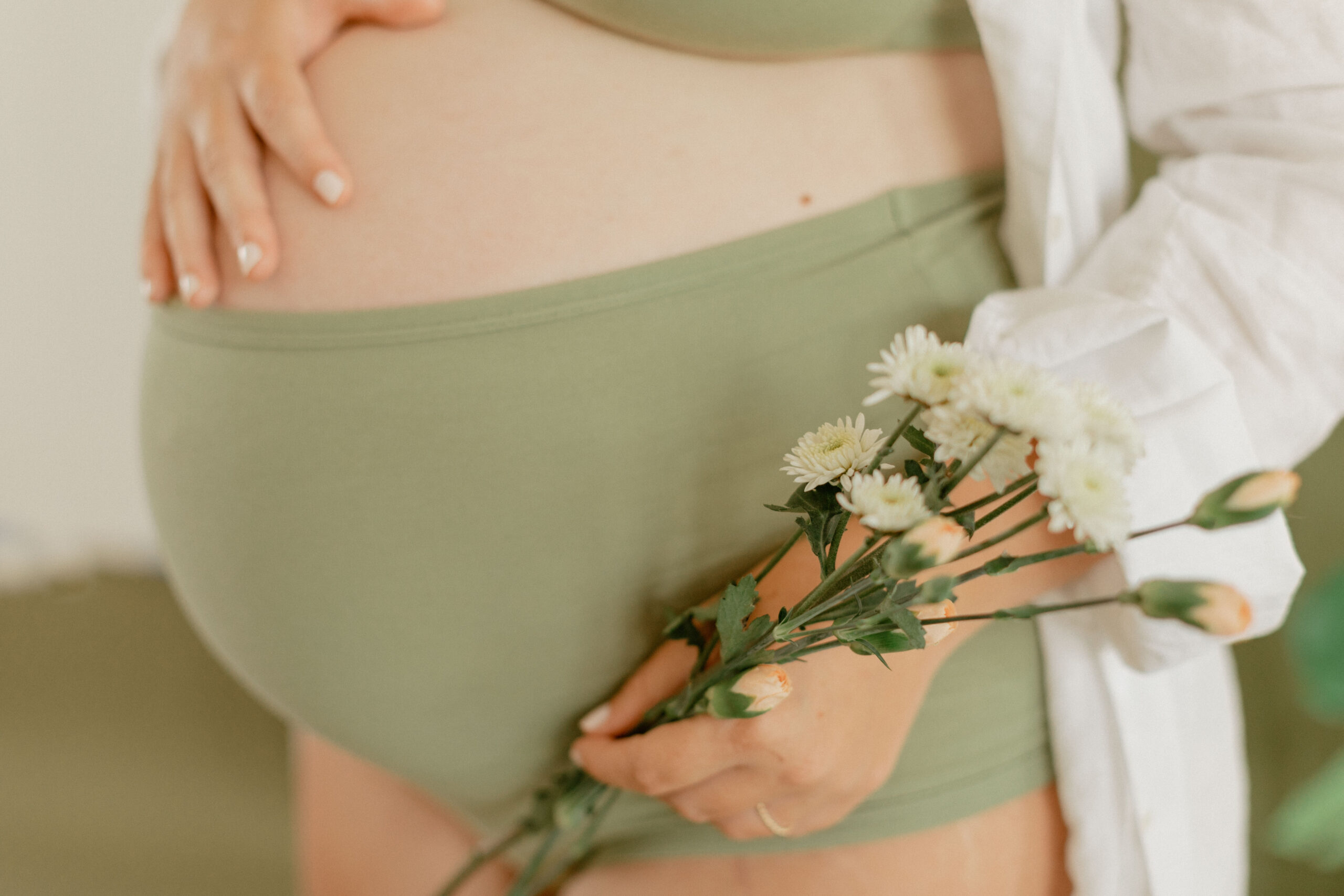 Editorial Maternity Session. Closeup of an expecting mother in green and a bouquet of flowers.